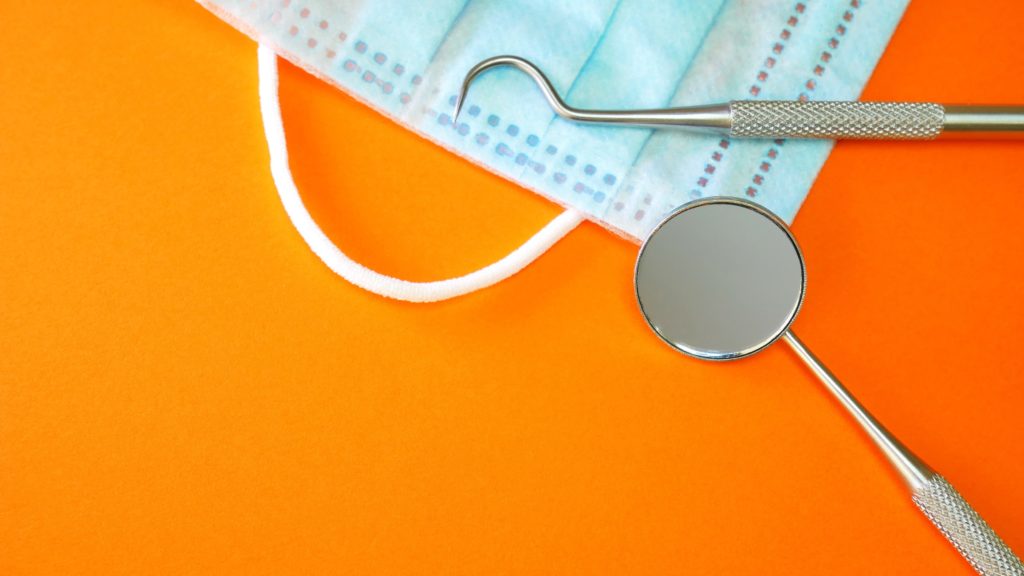 Dental tools and a mask laying on an orange background