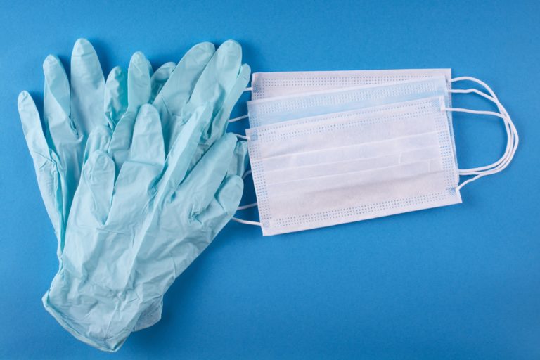 Blue surgical gloves and several masks lay on a blue background
