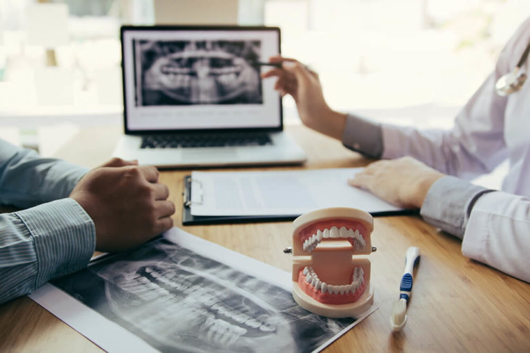 A dentist reviews dental x-rays with a patient while seated across a desk from each other